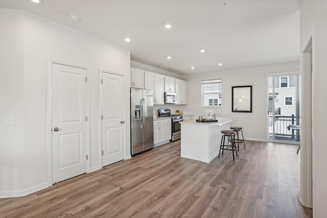 kitchen with white cabinets, appliances with stainless steel finishes, a center island, light hardwood / wood-style flooring, and a breakfast bar area