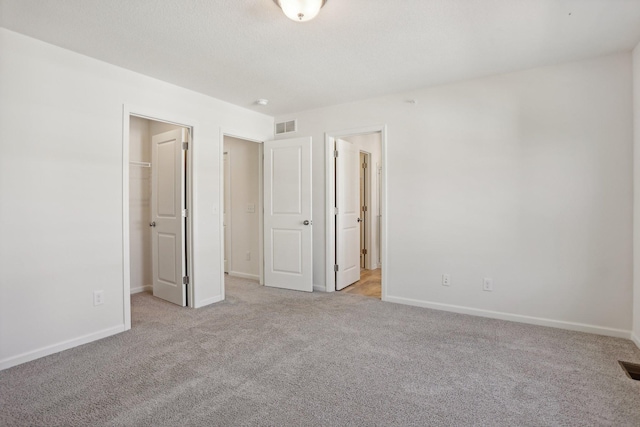 unfurnished bedroom featuring a walk in closet, light carpet, and a closet