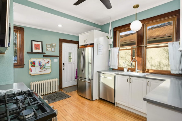 kitchen featuring appliances with stainless steel finishes, radiator heating unit, pendant lighting, white cabinetry, and sink