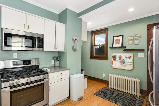 kitchen featuring white cabinetry, crown molding, light hardwood / wood-style flooring, appliances with stainless steel finishes, and radiator