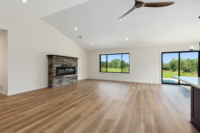 unfurnished living room with light wood-type flooring, ceiling fan with notable chandelier, a stone fireplace, and lofted ceiling