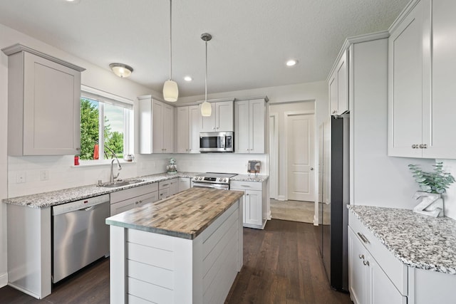 kitchen with hanging light fixtures, sink, a kitchen island, wood counters, and stainless steel appliances