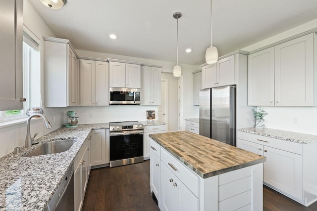 kitchen with appliances with stainless steel finishes, white cabinetry, sink, a kitchen island, and wood counters