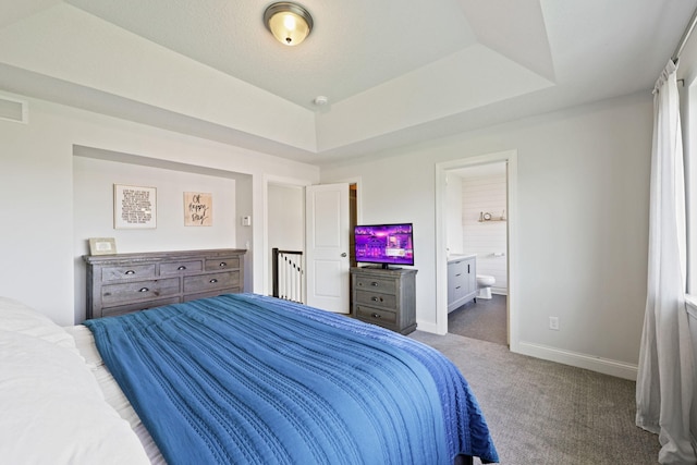 bedroom with connected bathroom, a raised ceiling, and dark colored carpet