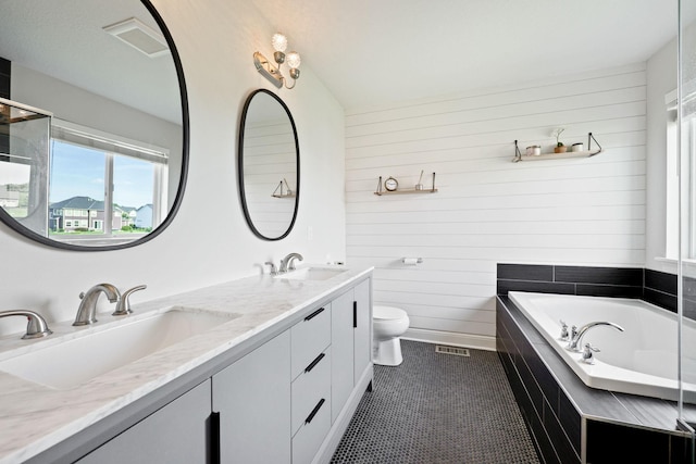 bathroom with tile patterned floors, toilet, a relaxing tiled tub, vanity, and wooden walls