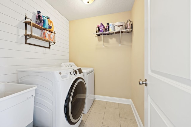 washroom featuring a textured ceiling, washing machine and dryer, sink, wood walls, and light tile patterned flooring