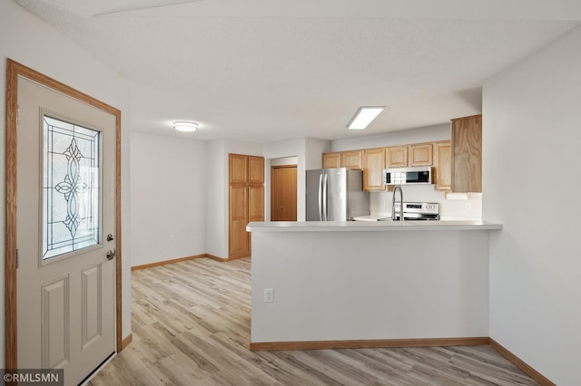 kitchen with appliances with stainless steel finishes, kitchen peninsula, light hardwood / wood-style floors, and light brown cabinets