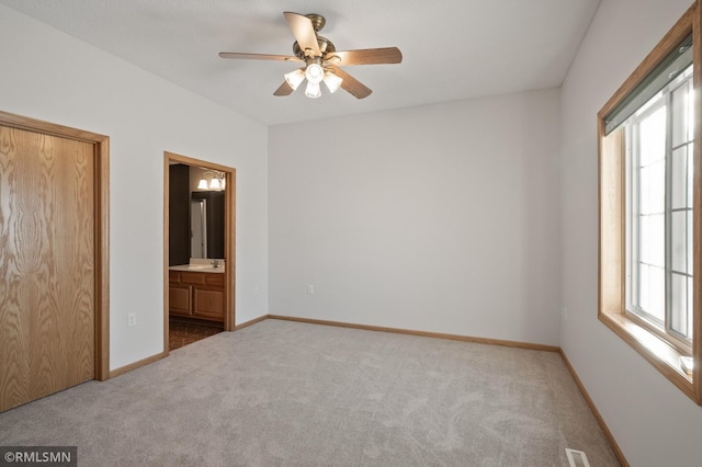 unfurnished bedroom with multiple windows, connected bathroom, carpet floors, and ceiling fan