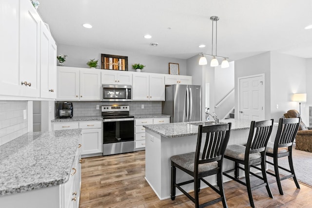 kitchen with sink, white cabinetry, stainless steel appliances, an island with sink, and decorative light fixtures