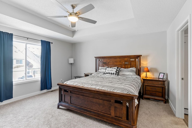 bedroom featuring ceiling fan, a tray ceiling, light carpet, and a textured ceiling