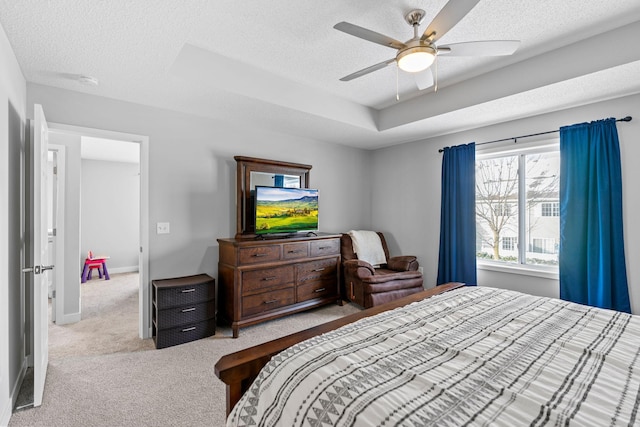 bedroom featuring ceiling fan, light colored carpet, a tray ceiling, and a textured ceiling