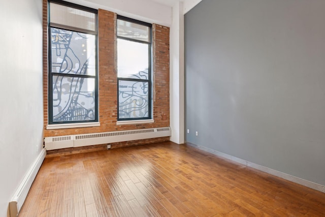 empty room featuring brick wall, a baseboard heating unit, radiator heating unit, and light wood-type flooring