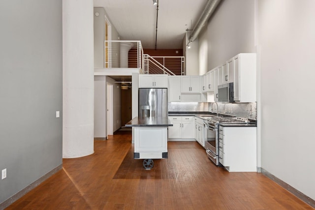 kitchen featuring appliances with stainless steel finishes, a high ceiling, tasteful backsplash, white cabinets, and a kitchen island