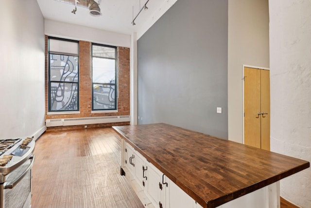 kitchen featuring butcher block countertops, a baseboard radiator, white cabinets, gas stove, and light hardwood / wood-style flooring