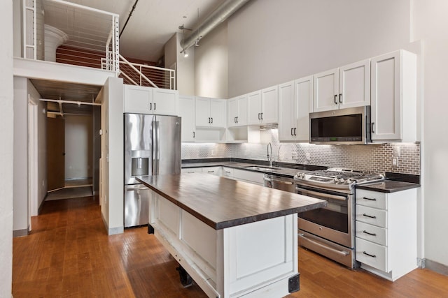 kitchen with appliances with stainless steel finishes, a high ceiling, white cabinets, dark hardwood / wood-style flooring, and a kitchen island