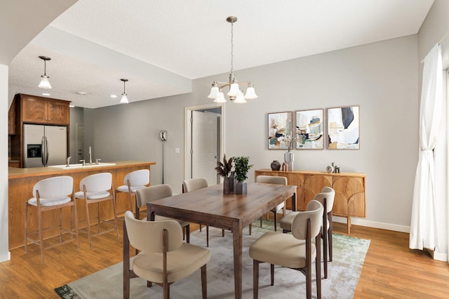 dining space featuring a notable chandelier, baseboards, a textured ceiling, light wood-style floors, and arched walkways