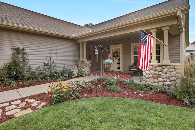 entrance to property with roof with shingles, a yard, and stone siding