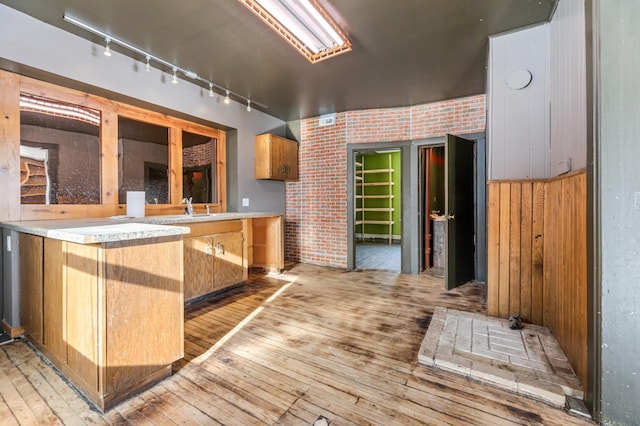 kitchen with brick wall, sink, light wood-type flooring, and wood walls