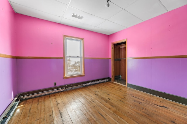 unfurnished room featuring wood-type flooring, a paneled ceiling, and a baseboard radiator