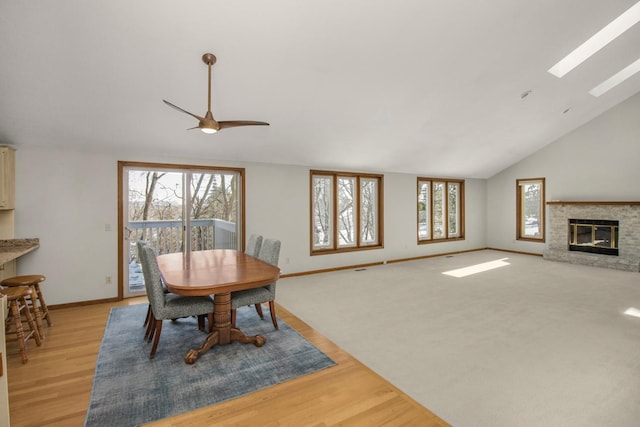 dining area featuring vaulted ceiling with skylight, a wealth of natural light, light hardwood / wood-style flooring, and a stone fireplace