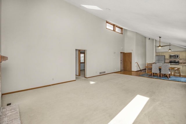 unfurnished living room featuring a skylight, high vaulted ceiling, and light colored carpet