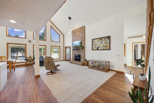 living room with a brick fireplace, wood-type flooring, and high vaulted ceiling