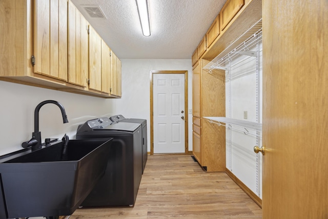 clothes washing area with sink, cabinets, light hardwood / wood-style floors, washer and dryer, and a textured ceiling