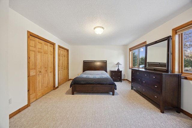 bedroom featuring multiple closets, light carpet, and a textured ceiling