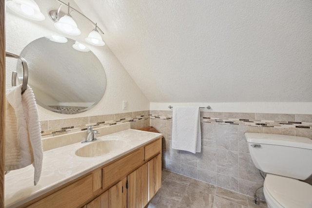 bathroom with vaulted ceiling, tile walls, vanity, toilet, and a textured ceiling