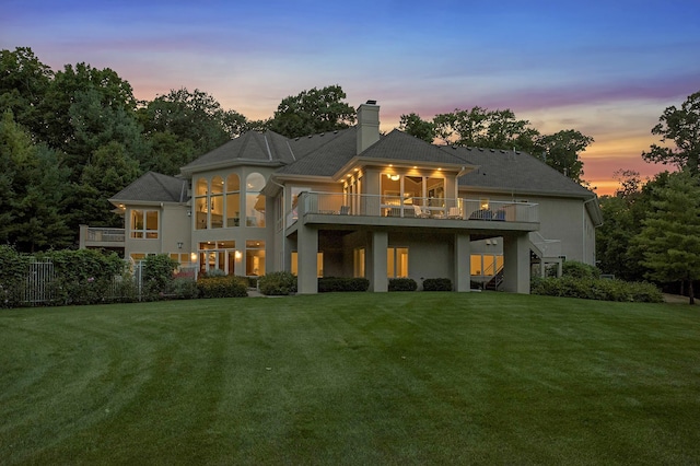 back house at dusk featuring a yard, a sunroom, and a deck