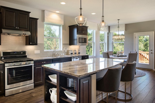 kitchen with light stone countertops, pendant lighting, appliances with stainless steel finishes, a kitchen island, and dark hardwood / wood-style floors