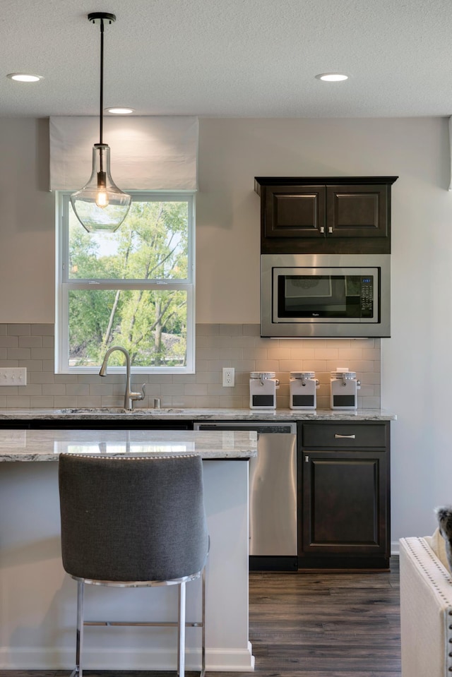 kitchen with decorative light fixtures, light stone counters, appliances with stainless steel finishes, and backsplash