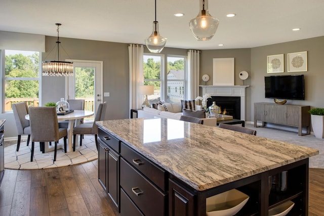 kitchen with dark brown cabinetry, a center island, decorative light fixtures, a healthy amount of sunlight, and light stone counters