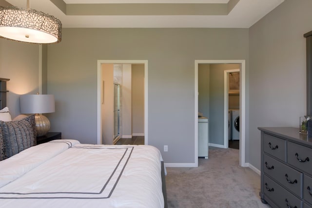 bedroom with a tray ceiling, ensuite bathroom, washer / dryer, and light carpet