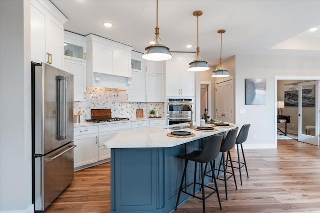 kitchen featuring decorative light fixtures, white cabinetry, stainless steel appliances, light wood-type flooring, and a center island with sink