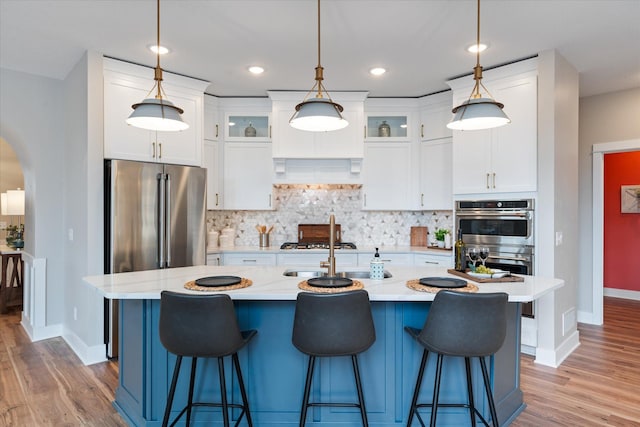 kitchen with a kitchen island with sink, white cabinetry, pendant lighting, and stainless steel appliances