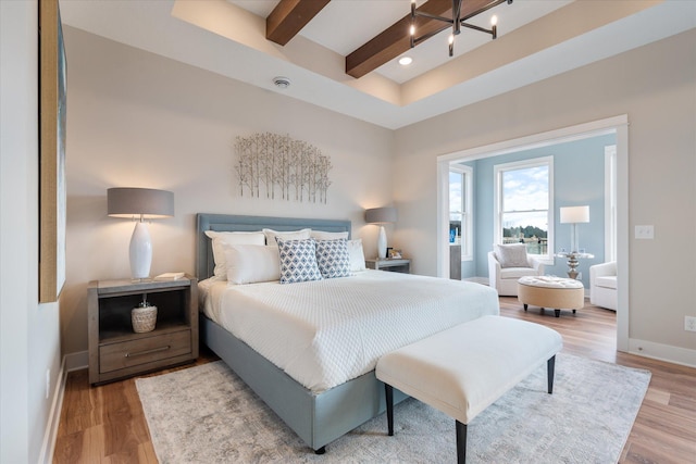 bedroom with hardwood / wood-style floors, beam ceiling, and an inviting chandelier