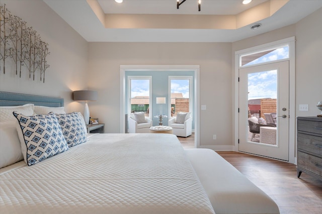 bedroom featuring light hardwood / wood-style flooring, a tray ceiling, and access to outside