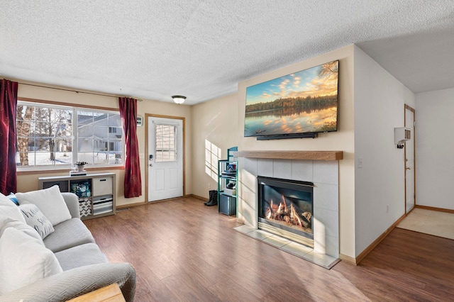 living room featuring a tiled fireplace, a textured ceiling, and wood-type flooring