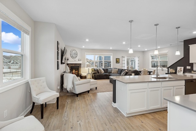 kitchen with decorative light fixtures, dishwasher, sink, white cabinets, and light wood-type flooring