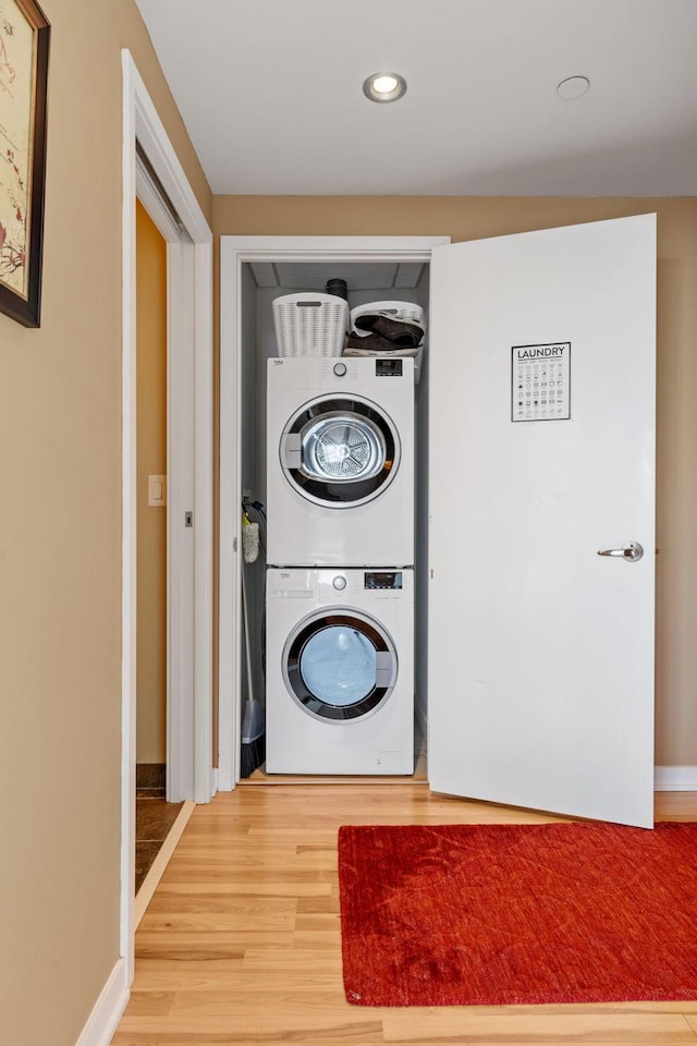 laundry room with wood-type flooring and stacked washer / dryer