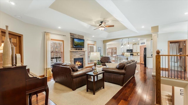 living room featuring decorative columns, a stone fireplace, a raised ceiling, and light wood-style flooring