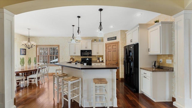 kitchen with dark countertops, black appliances, dark wood-type flooring, and wallpapered walls