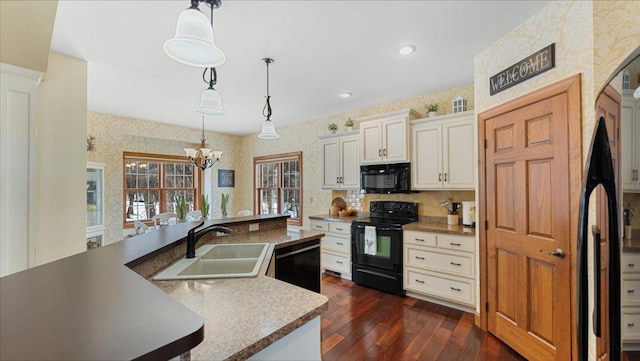 kitchen featuring dark wood-style floors, decorative light fixtures, a sink, black appliances, and wallpapered walls