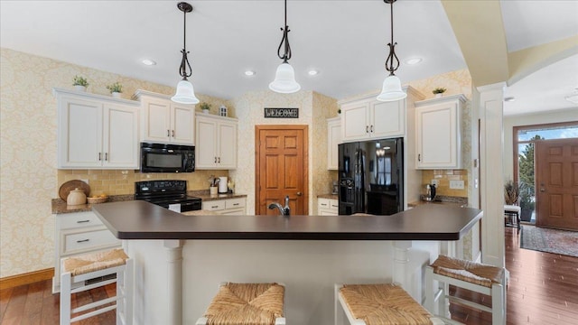 kitchen with black appliances, dark wood-type flooring, a kitchen bar, and wallpapered walls