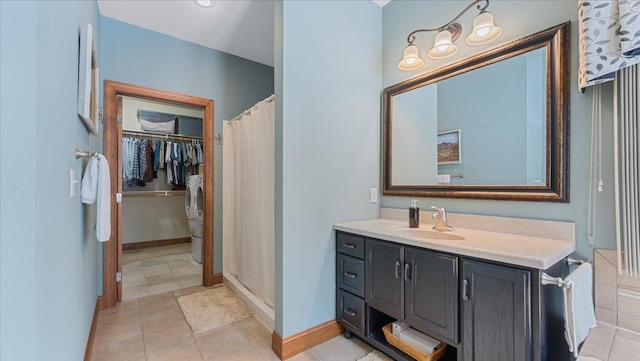 bathroom with a walk in closet, a stall shower, vanity, washer / dryer, and baseboards