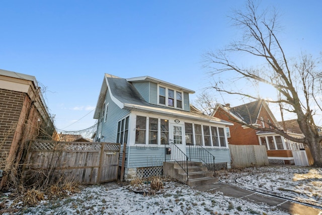 snow covered rear of property with a sunroom