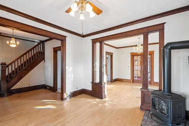 unfurnished living room with ornate columns, a wood stove, ornamental molding, hardwood / wood-style flooring, and ceiling fan with notable chandelier