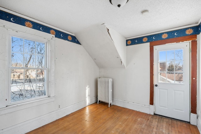 additional living space featuring radiator heating unit, wood-type flooring, a textured ceiling, and a wealth of natural light