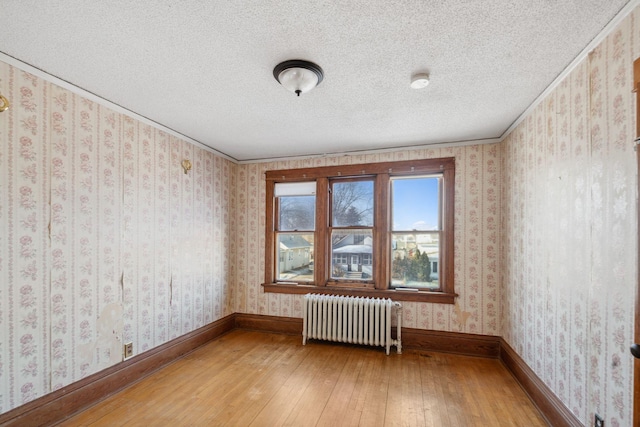 empty room with radiator heating unit, wood-type flooring, and a textured ceiling